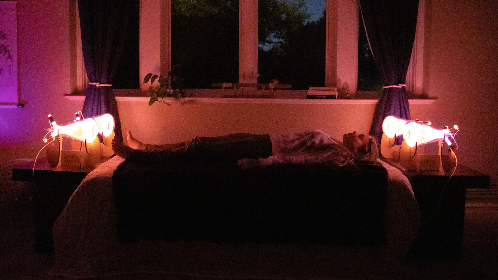 dimly lit room with a woman laying on a bed between the Theraphi bulbs