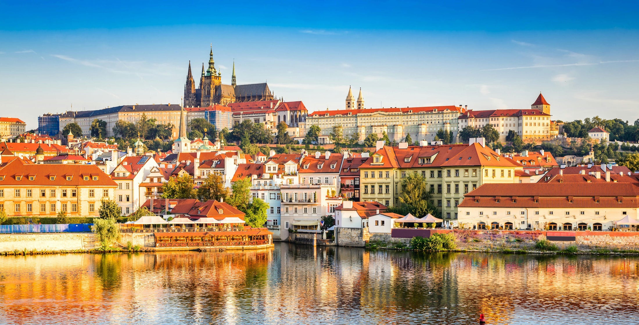 Cityscape of Prague with notable buildings and a river in the foreground